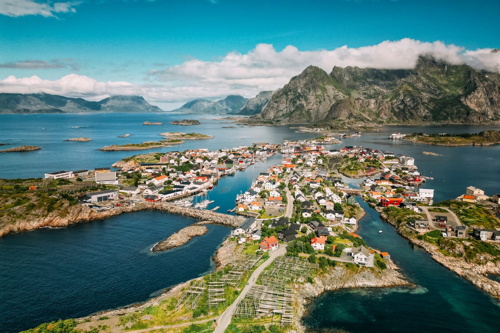 An aerial view of a fishing village spread across rocky islands beneath steep mountains.