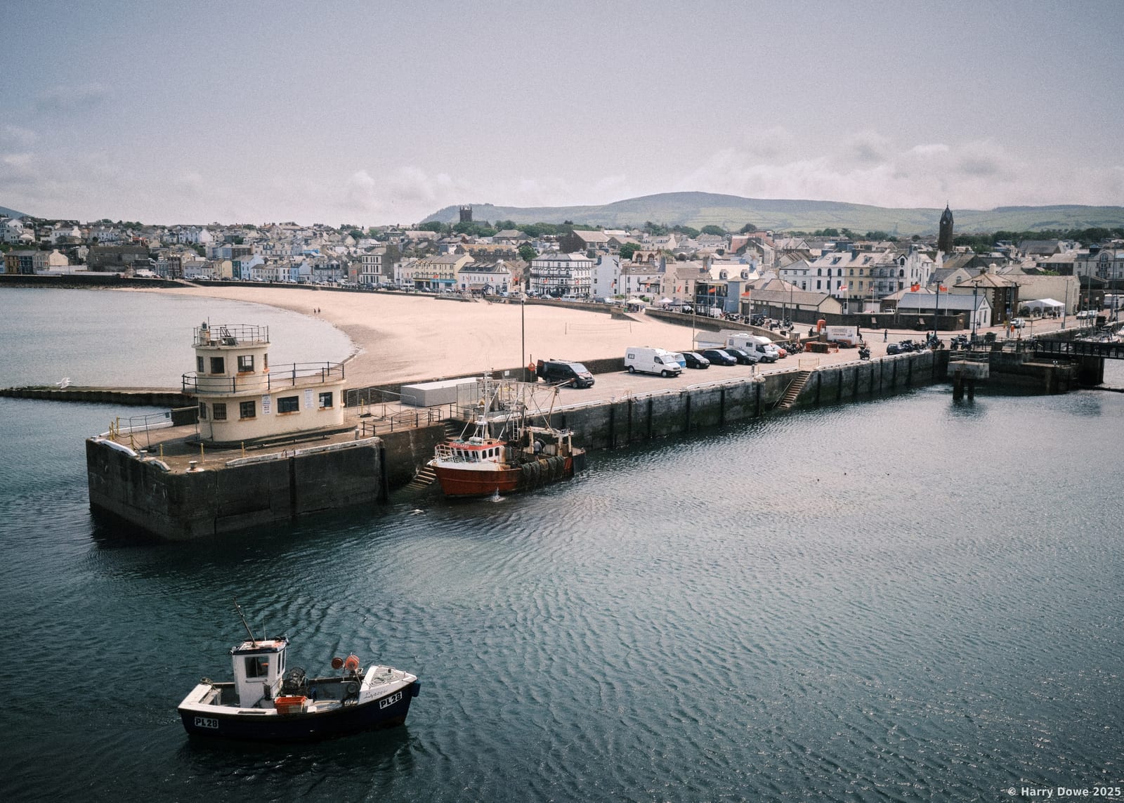 High angle view of Peel breakwater and harbour with fishing boats moored near a sandy beach and coastal town on the Isle of Man