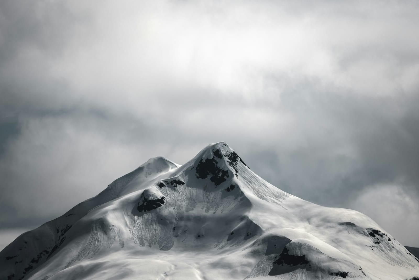 A sculpted snow-covered mountain rising beneath heavy grey clouds.