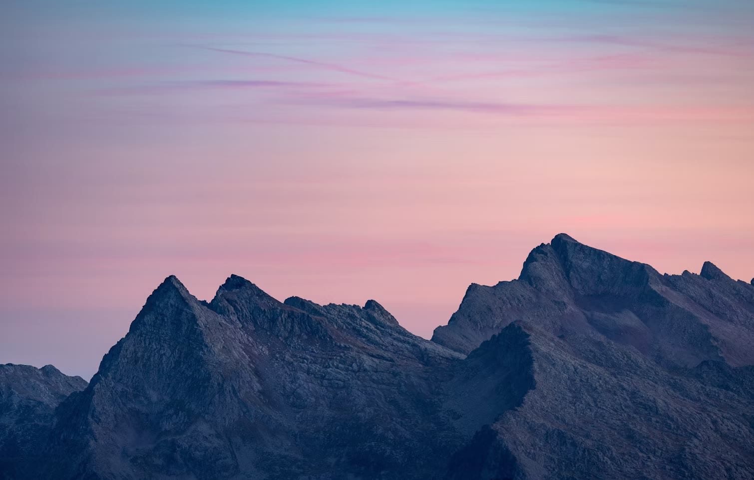 A jagged mountain ridge silhouetted beneath a pastel pink and blue evening sky.
